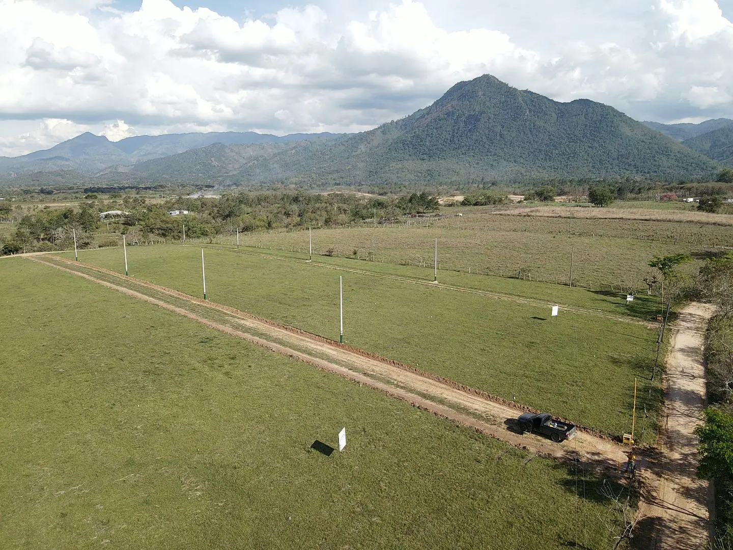 Vista aérea del terreno: calles abiertas, postes de luz y los lotes en zacate, con la montaña al fondo